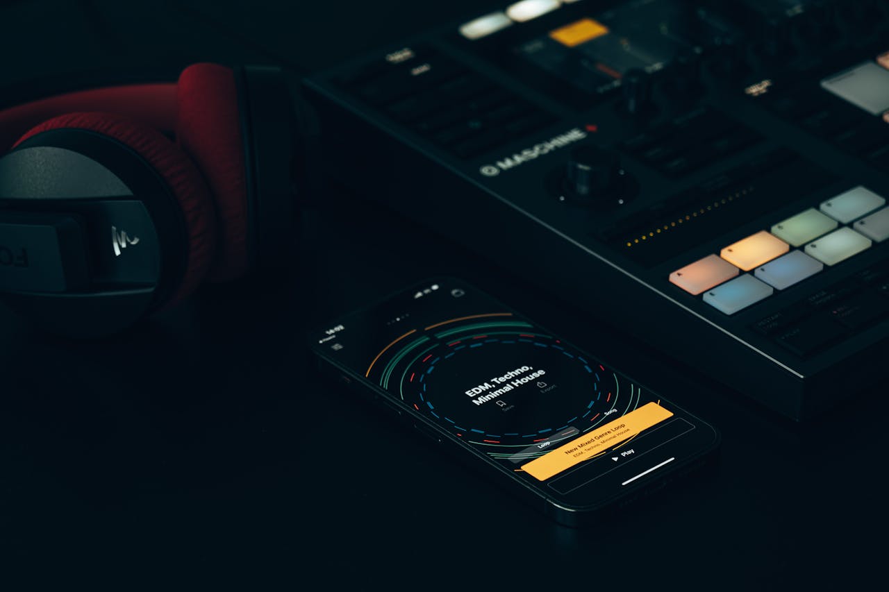 Dark-themed music setup featuring a DJ controller, smartphone, and headphones on a sleek surface.