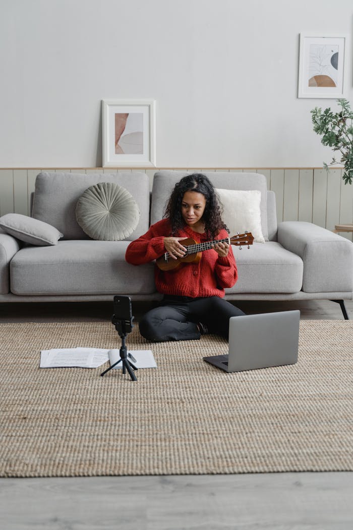 Young woman giving an online ukulele lesson while sitting on the floor in a cozy living room.